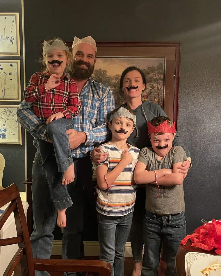 Dr. Kaci Kuykendall, her husband Dustin, and their three children wearing paper crowns and stick-on mustaches after a family dinner